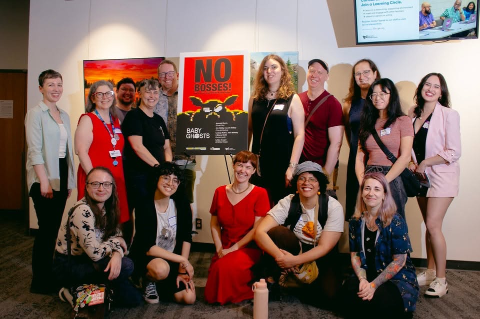 Photo from the No Bosses Round Table with hosts surrounding poster for the event